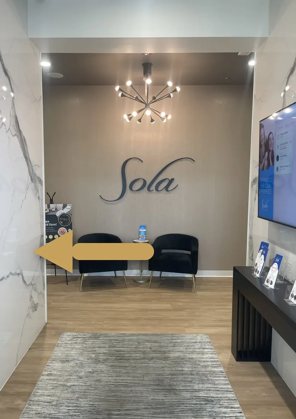 Lobby at Sola Salon Studios on Upper Peach Street in Erie, PA, with a gold arrow pointing left past the two black chairs toward Formosa Hair Studio